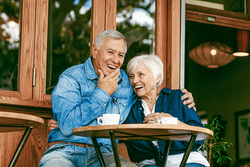 A close-up of a smiling senior couple sitting outdoors at a cafe table.